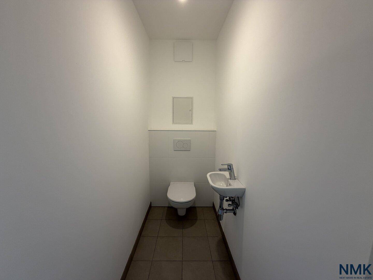 Modernes Gäste-WC mit wandhängender Toilette, kleinem Waschbecken und Fliesenboden.