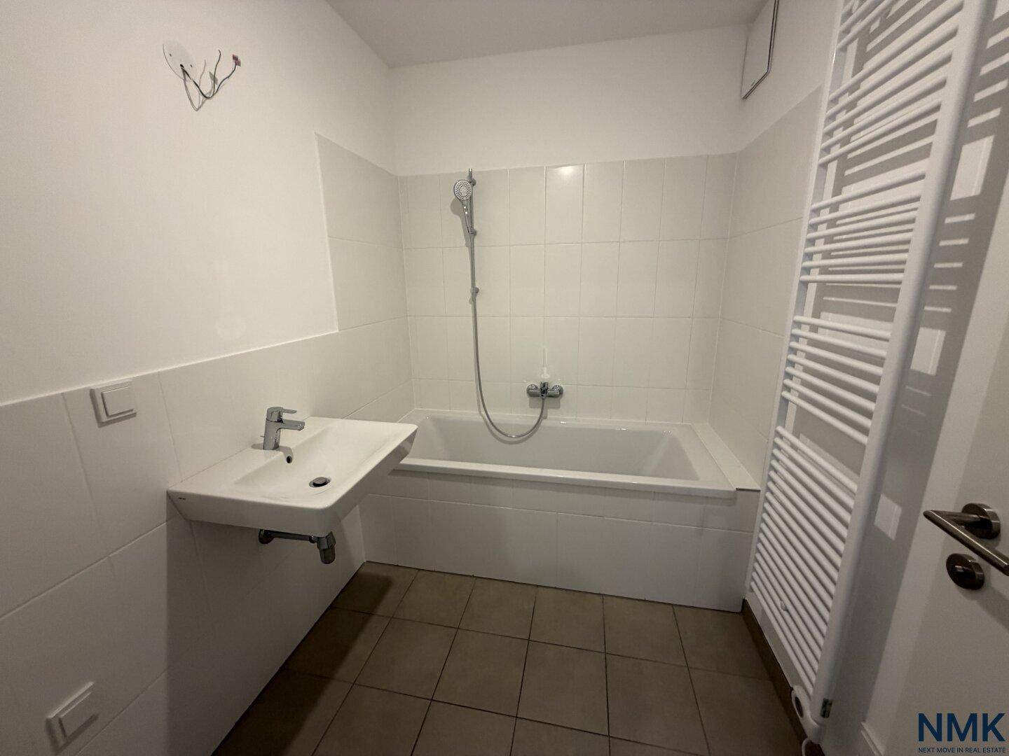 Helles Badezimmer mit Badewanne, Waschbecken und praktischem Handtuchheizkörper.