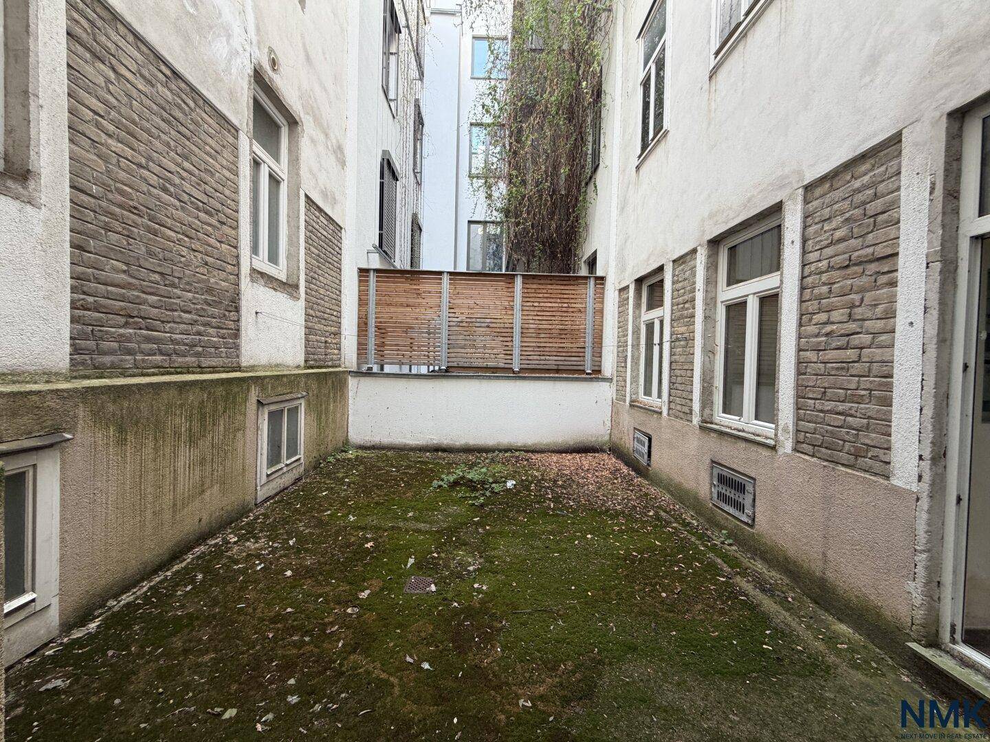 Unrenovierter Innenhof mit Moosbewuchs und schmutzigen Wänden, zeigt den Zustand vor der Sanierung.