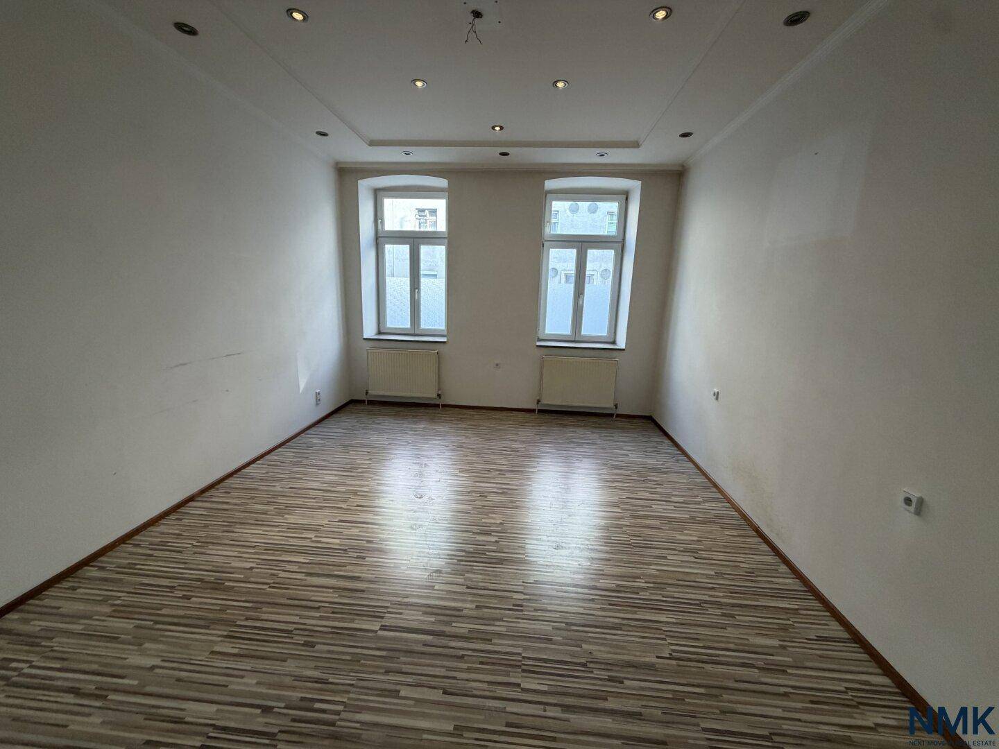 Unmöbliertes Wohnzimmer vor der Sanierung mit Laminatboden und sichtbaren Heizkörpern.