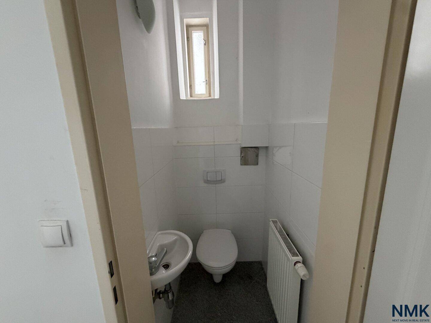 Einfaches Gäste-WC mit kleinem Waschbecken, Toilette und weiß gefliesten Wänden, renovierungsbedürftig.