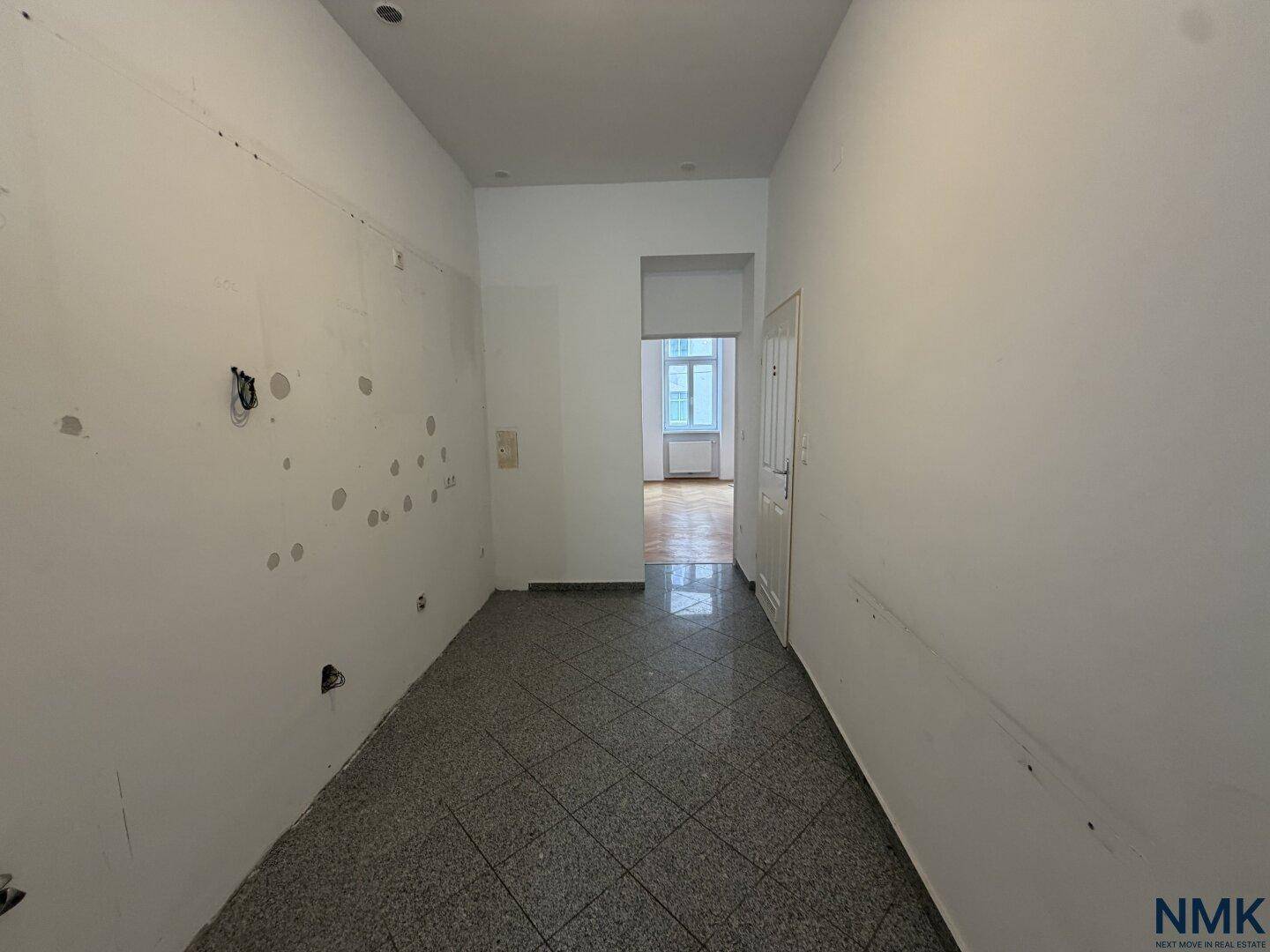 Leerer Raum mit grauen Fliesen und vorbereiteten Wänden, ideal für eine neue Kücheninstallation.