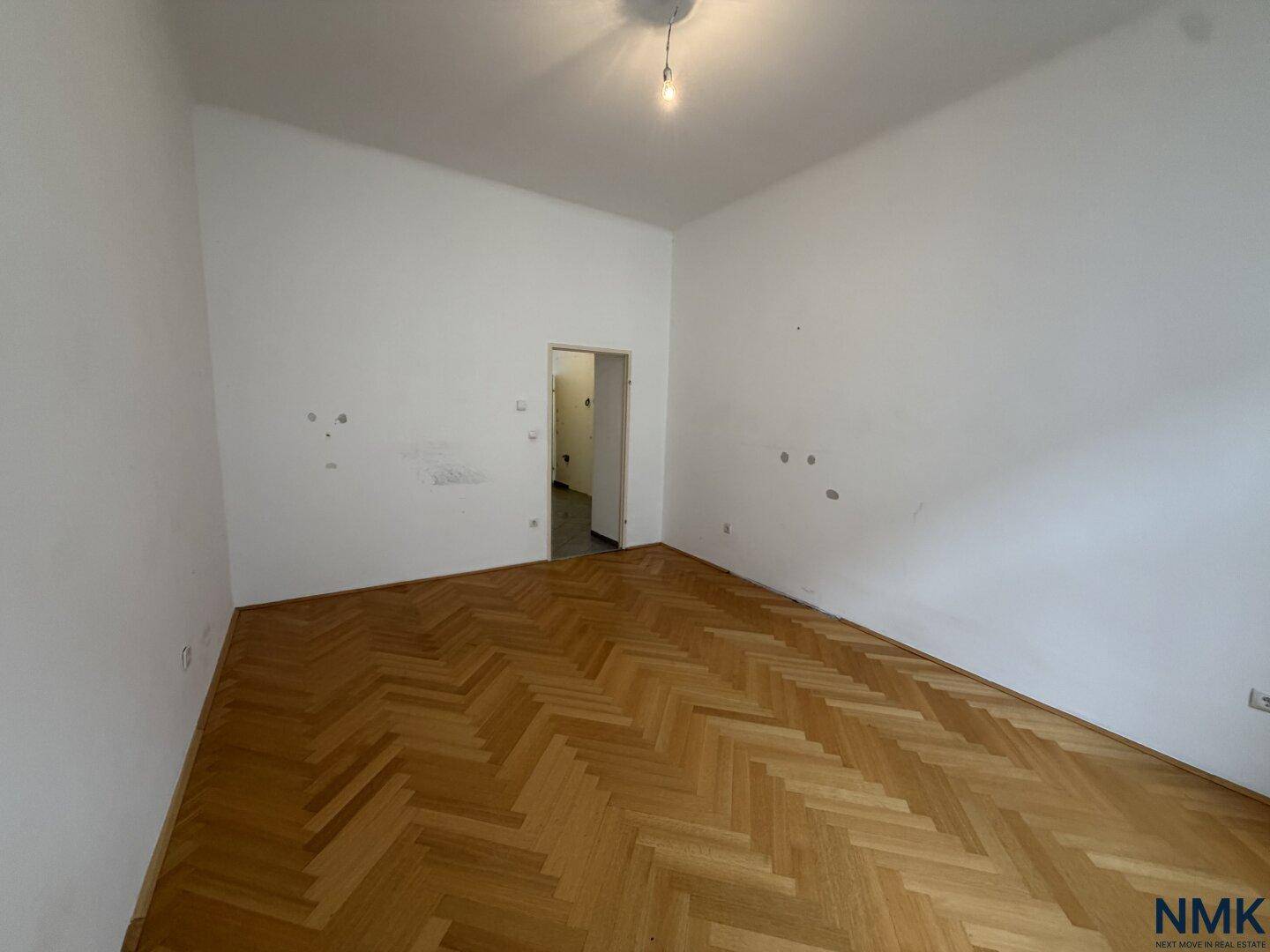 Leeres Zimmer mit Fischgrätparkett und weißen Wänden, bietet vielseitige Nutzungsmöglichkeiten.