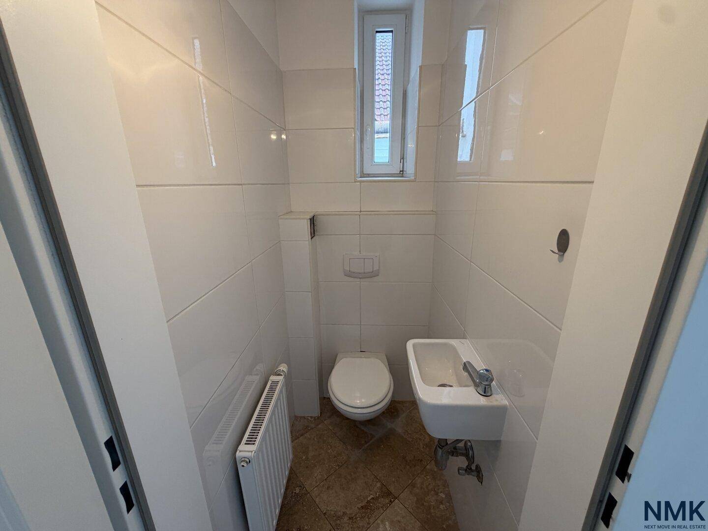Gäste-WC mit weißen Fliesen, wandhängendem WC und kleinem Waschbecken, vor der Modernisierung.
