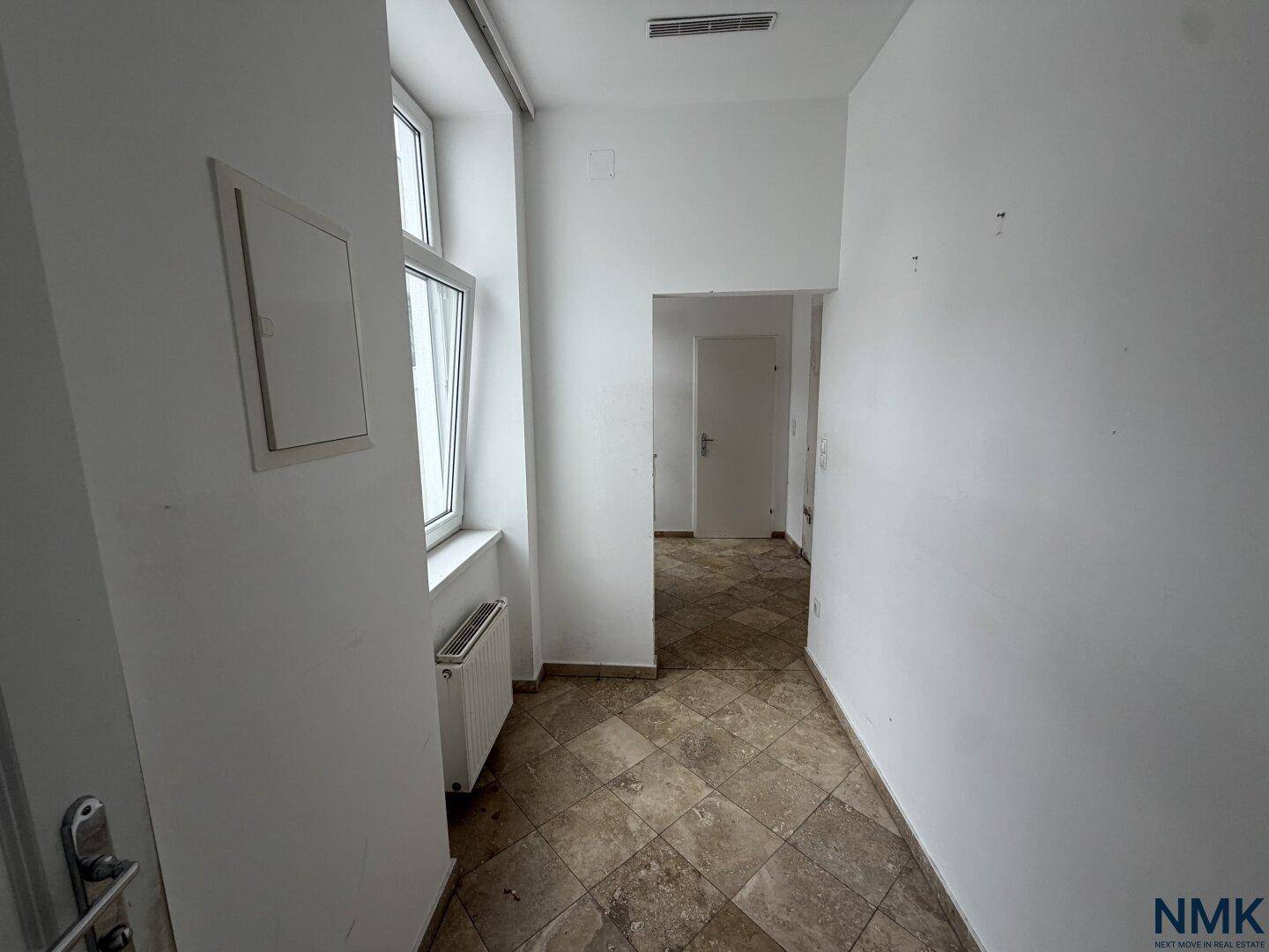 Flur mit Fliesenboden, Heizkörper und Fenster, der eine Sanierung benötigt.