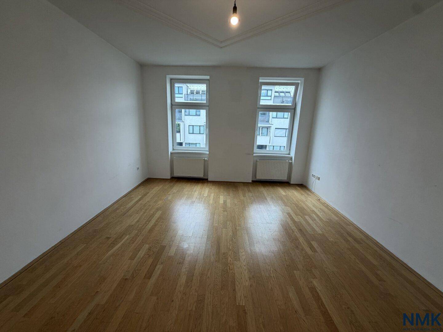 Leeres Wohnzimmer mit Holzparkettboden und zwei Fenstern, bereit für die individuelle Gestaltung.
