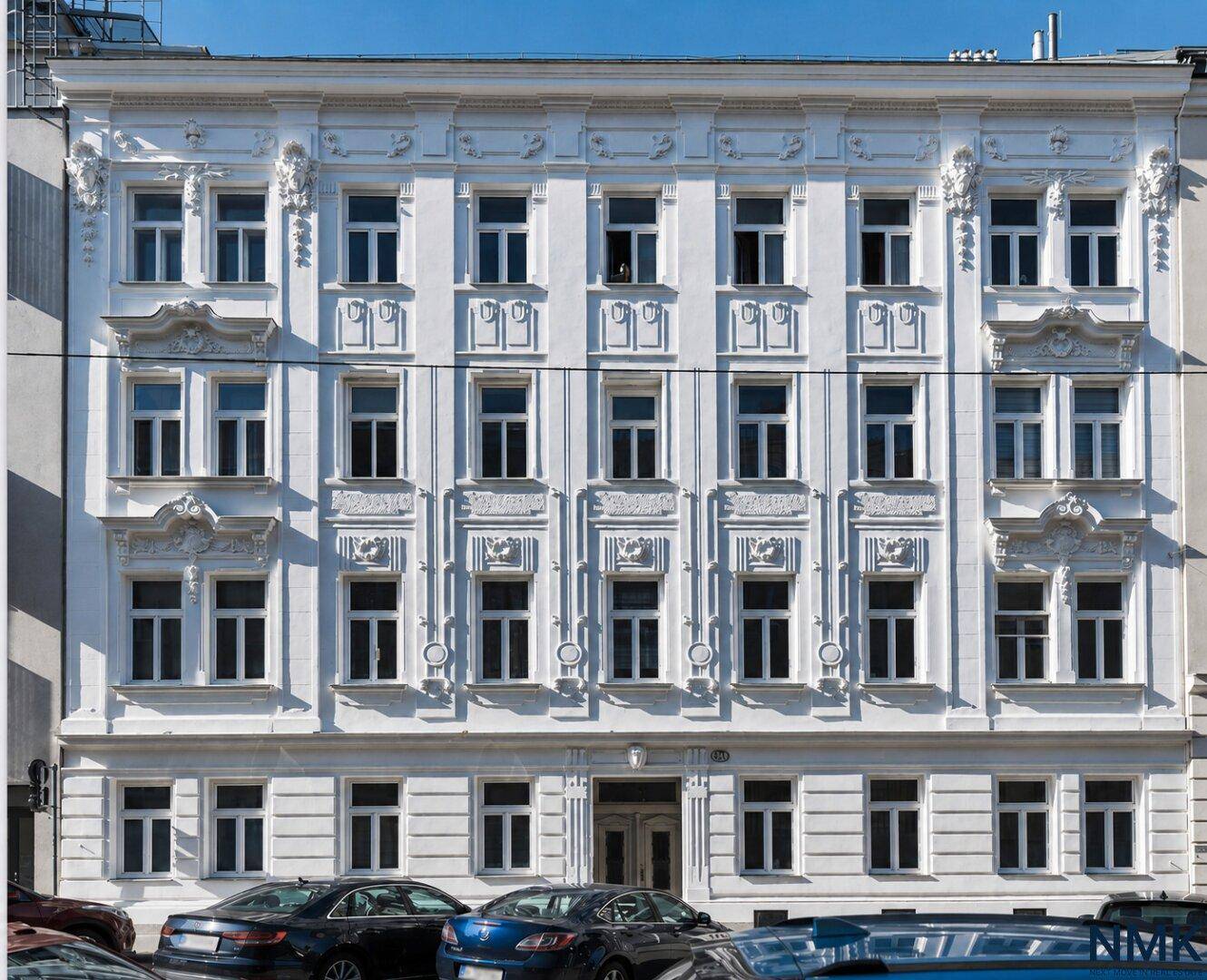 Eindrucksvolle weiße Fassade eines Altbaus mit reich verzierten Details und großen Fenstern.