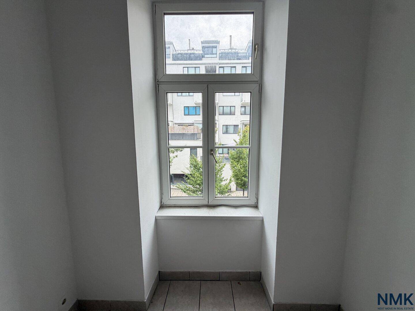 Dachfenster in einem Raum mit schrägen Wänden und Blick auf umliegende Gebäude.