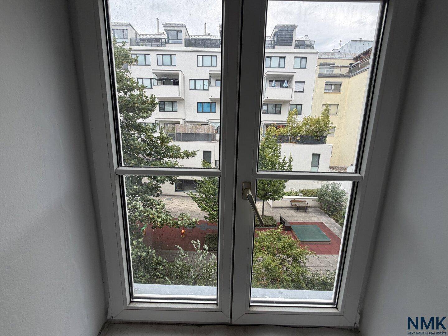 Großes Fenster mit Blick auf einen grünen Innenhof und einen Spielplatzbereich.
