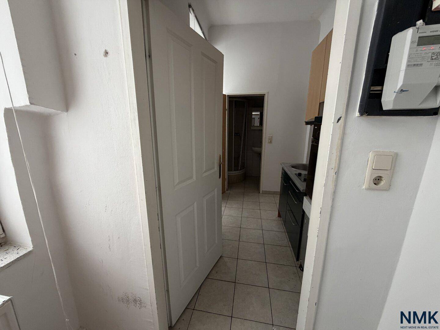 Kleine Küche mit Fliesenboden und Blick auf ein Badezimmer, funktional eingerichtet.