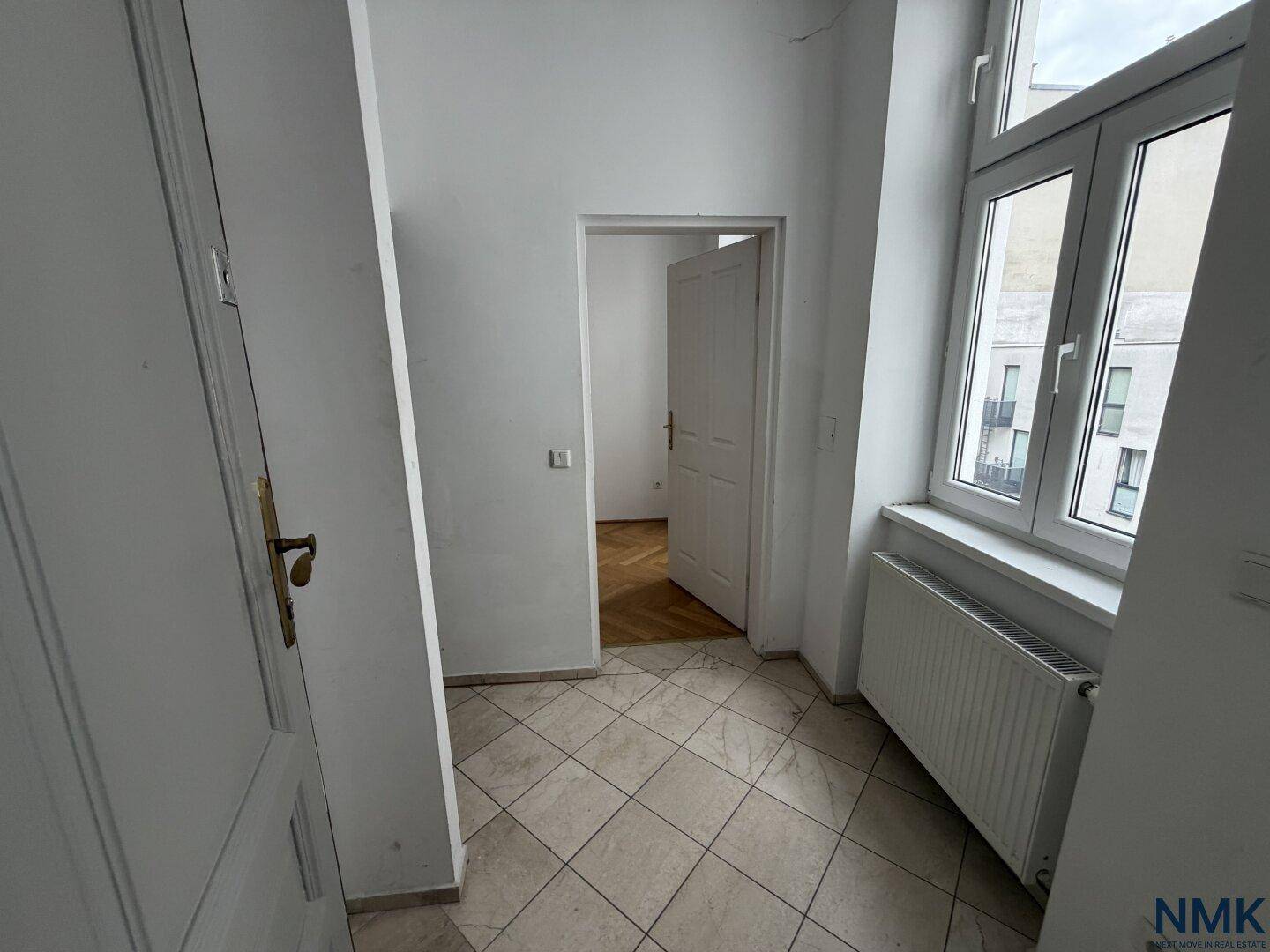 Flur mit Fliesenboden, Fenster und Zugang zu weiteren Räumen.
