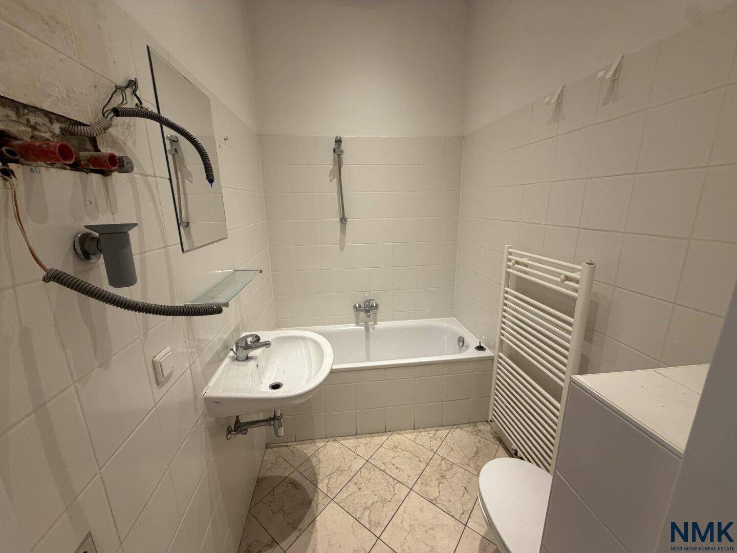 Badezimmer mit Badewanne, Waschbecken und Heizkörper, renovierungsbedürftig.