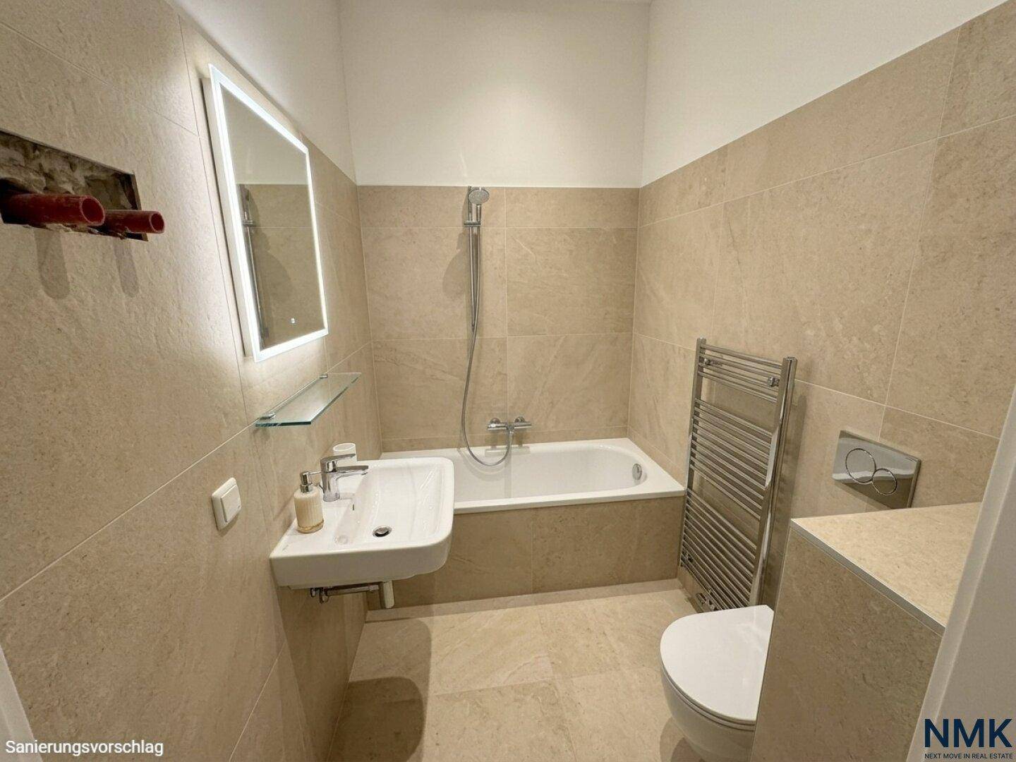 Modernisiertes Badezimmer mit beigefarbenen Fliesen, Badewanne und beleuchtetem Spiegel.