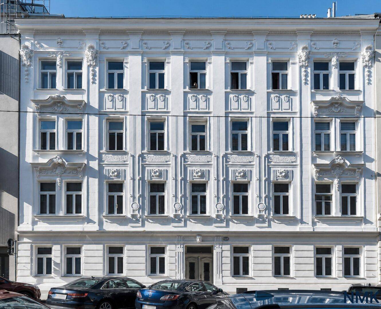 Historische weiße Fassade eines Altbaus mit vielen Fenstern und dekorativen Elementen.