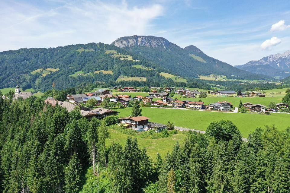 Panoramablick auf ein malerisches Dorf in einer grünen Berglandschaft mit bewaldeten Hängen.