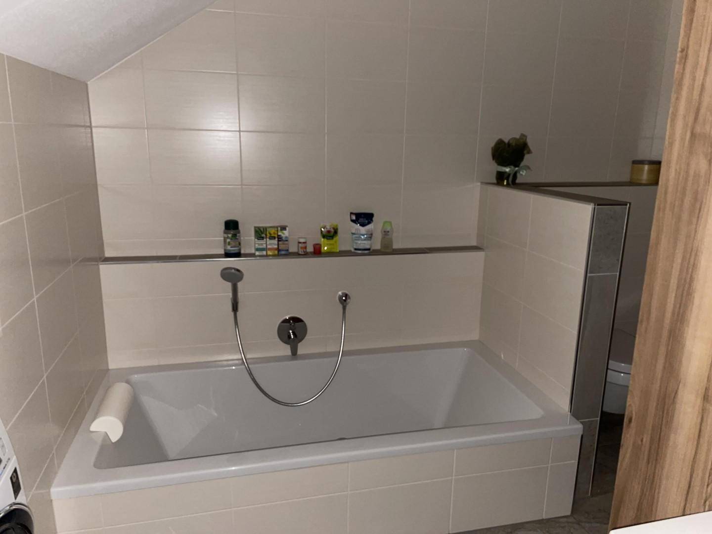 Helles Badezimmer mit integrierter Badewanne und beigefarbenen Fliesen an Wänden und Boden.