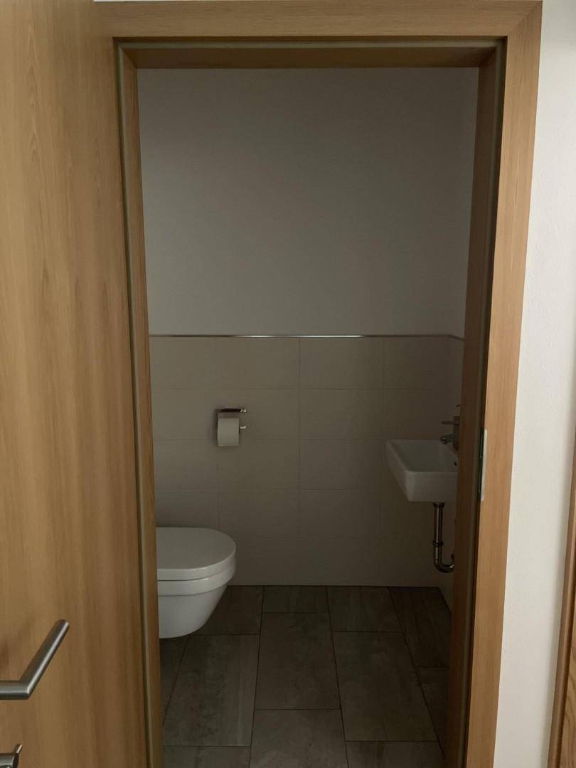 Kleines Gäste-WC mit wandhängender Toilette, Waschbecken und hellen Fliesen.