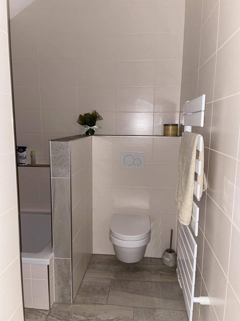 Modernes Badezimmer mit wandhängendem WC, beigefarbenen Fliesen und Handtuchheizkörper.