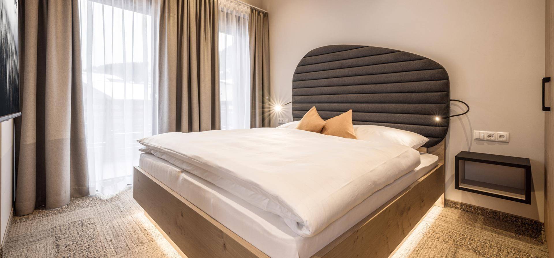 Modernes Schlafzimmer mit großem Doppelbett, indirekter Beleuchtung und Zugang zum Balkon.
