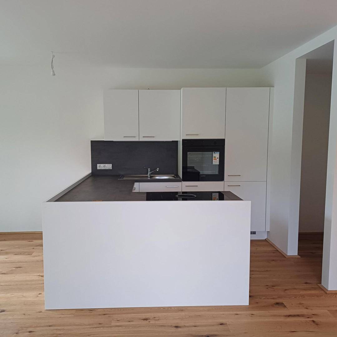 Neue, moderne Küche mit weißen Schränken, Kochinsel und Eichenparkettboden.