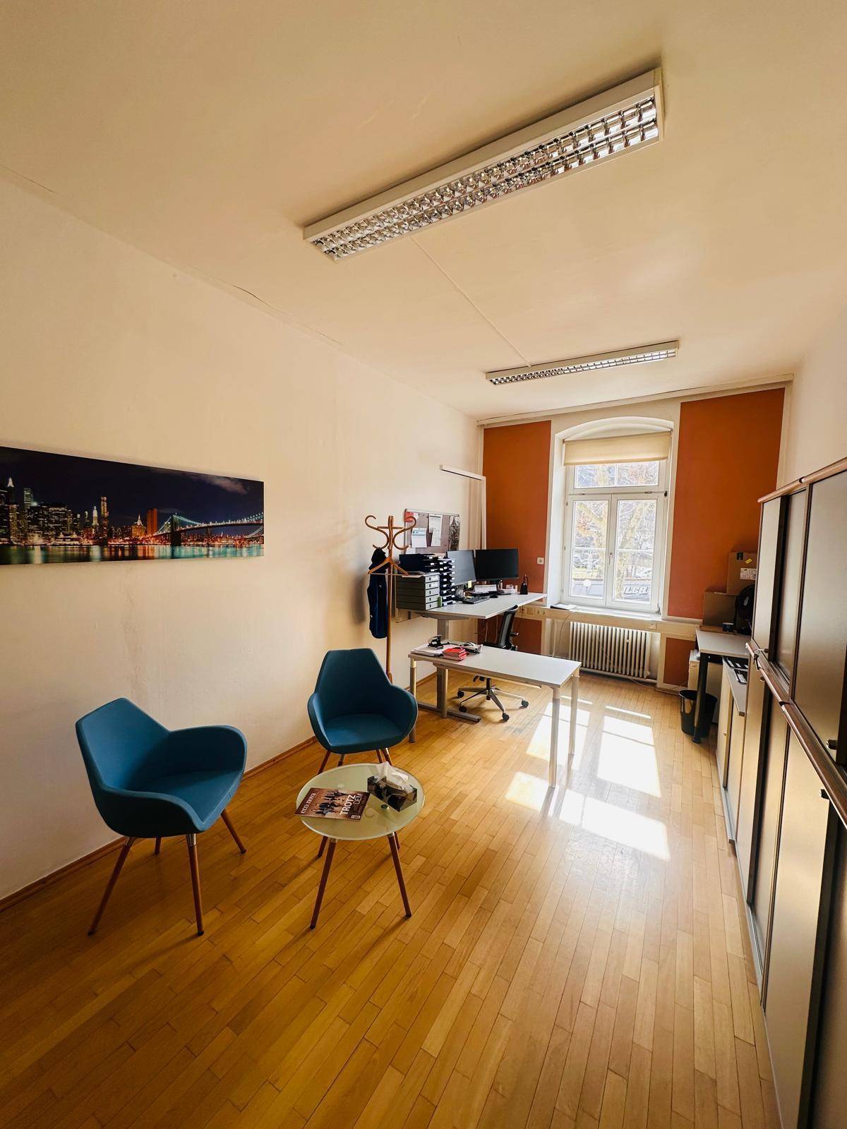 Modern eingerichtetes Büro mit Holzfußboden, Schreibtisch und blauen Stühlen im Wartebereich.