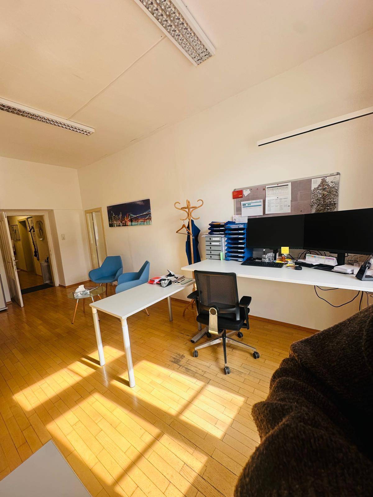 Geräumiges Büro mit Holzfußboden, mehreren Arbeitsplätzen und einem kleinen Wartebereich.