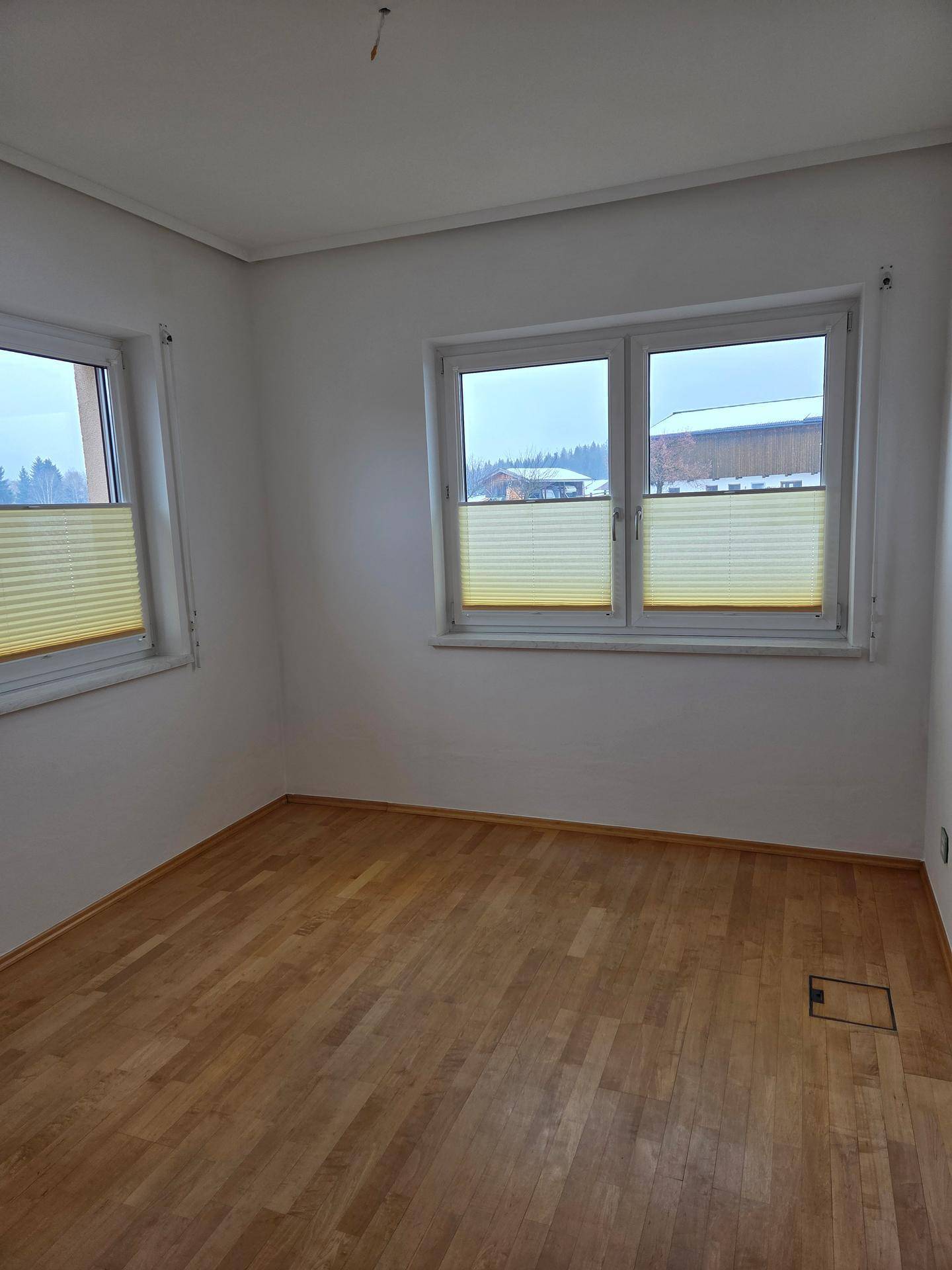 Heller Raum mit Holzboden und mehreren Fenstern, die viel Tageslicht hereinlassen.