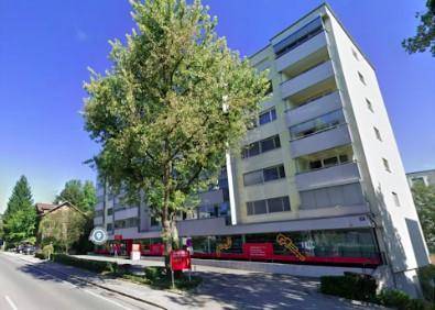 Modernes Mehrfamilienhaus mit Geschäften im Erdgeschoss und einem großen Baum im Vordergrund.