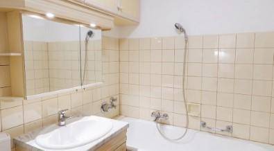 Badezimmer mit beigen Fliesen, Waschbecken, Spiegelschrank und Badewanne mit Duschfunktion.