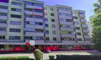 Mehrfamilienhaus mit mehreren Balkonen und Geschäften im Erdgeschoss, von der Straße aus gesehen.