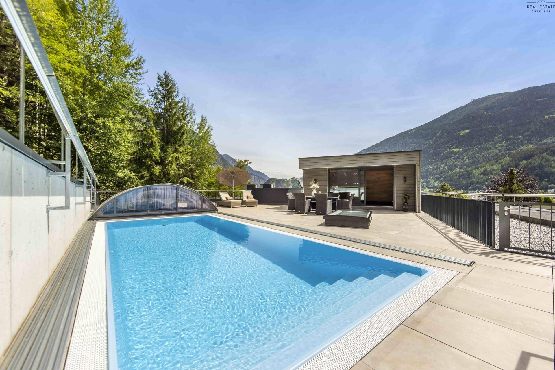 Außenbereich mit großem Pool, Liegestühlen und Bergblick, umgeben von üppiger Vegetation.