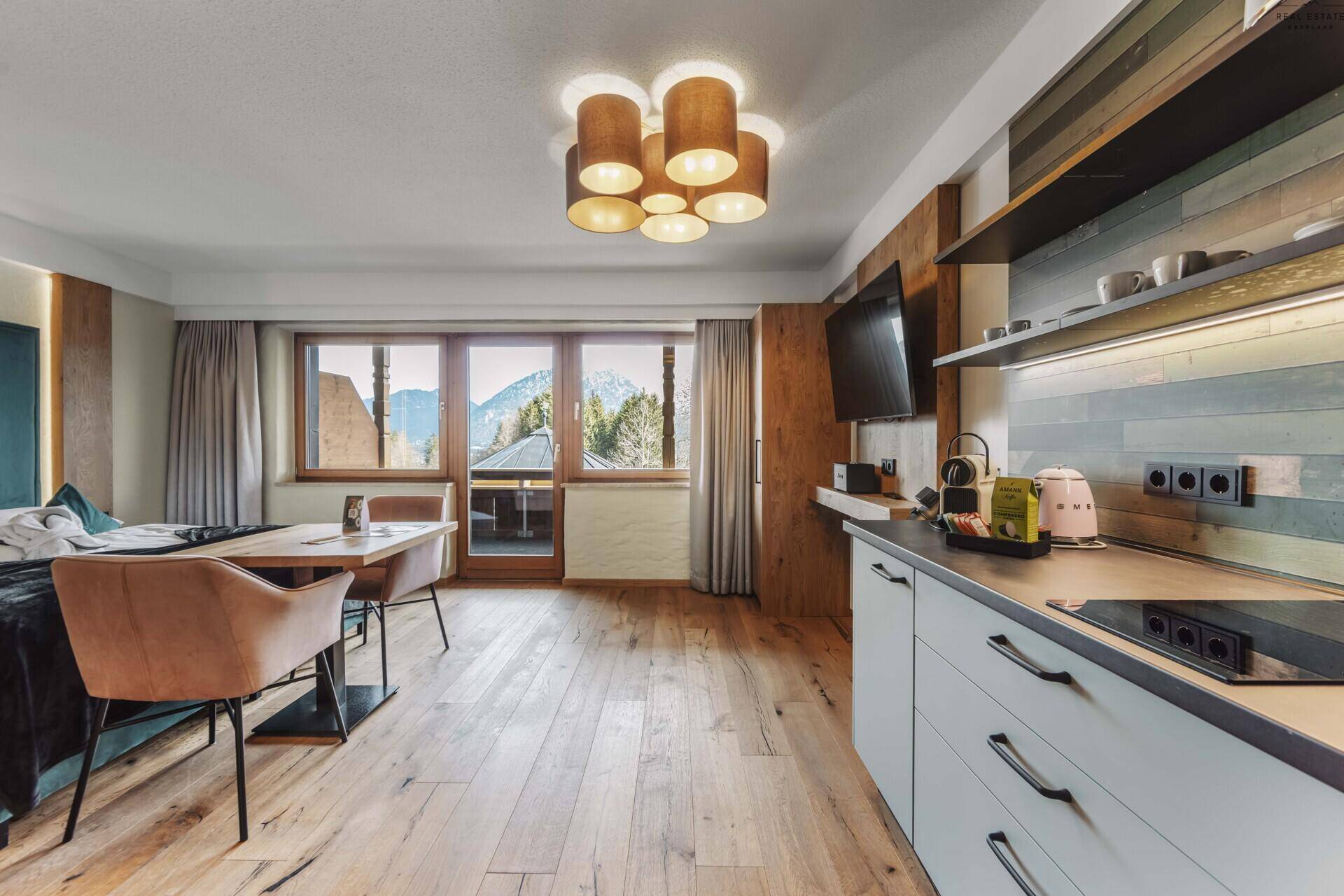 Offener Wohn-Schlafbereich mit Küchenzeile, Holzboden und Panoramablick auf die Berge.