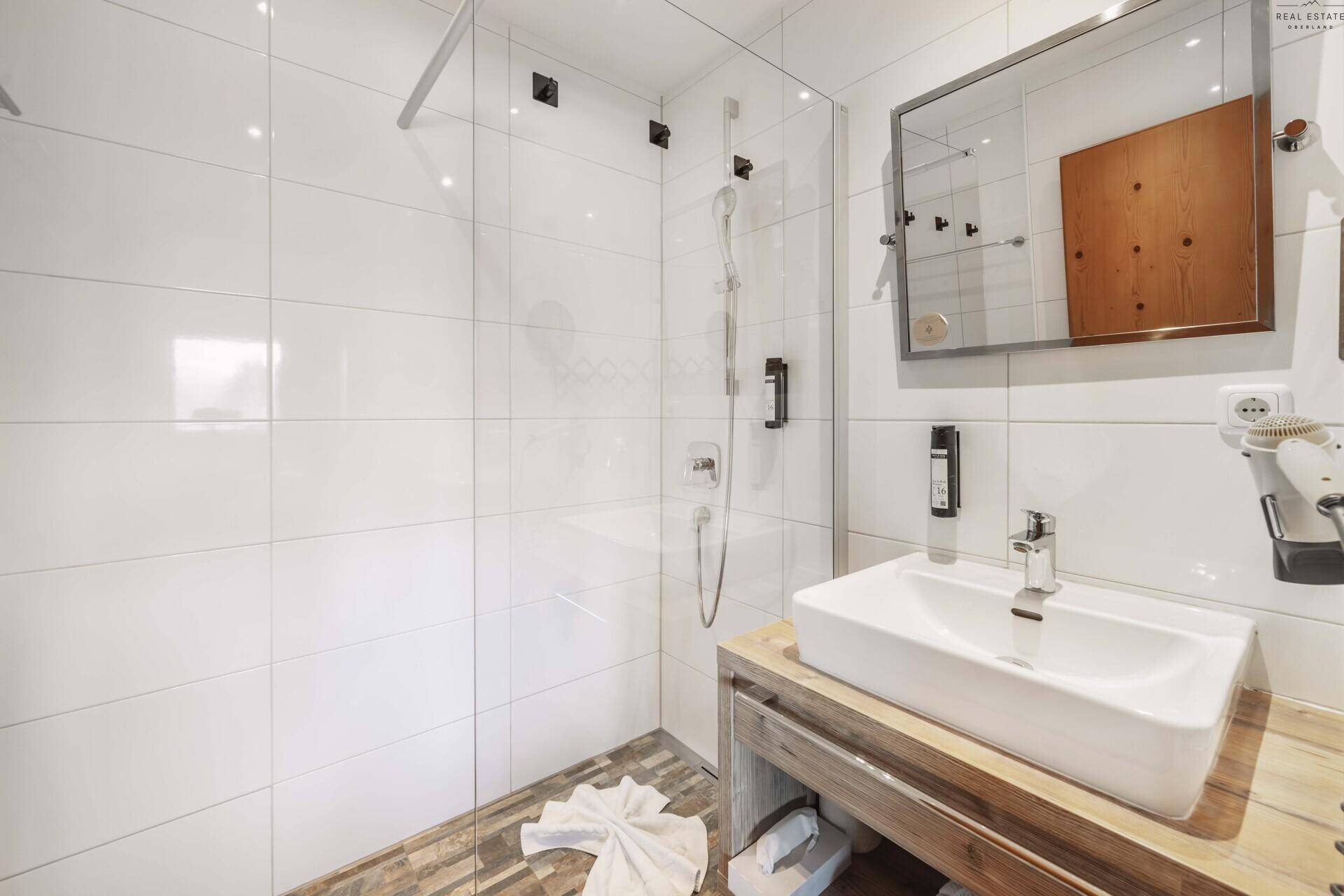 Modernes Badezimmer mit weißen Fliesen, ebenerdiger Dusche und Holzwaschtisch.