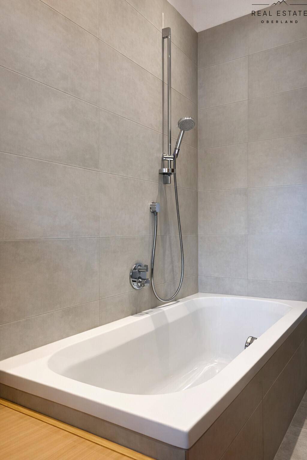 Eingebaute Badewanne mit Duscharmatur in einem modern gefliesten Badezimmer.
