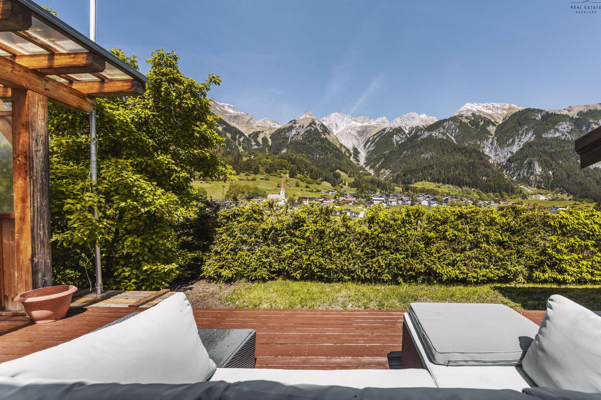 Entspannungsbereich auf der Terrasse mit Blick über eine Hecke auf die majestätischen Berge.