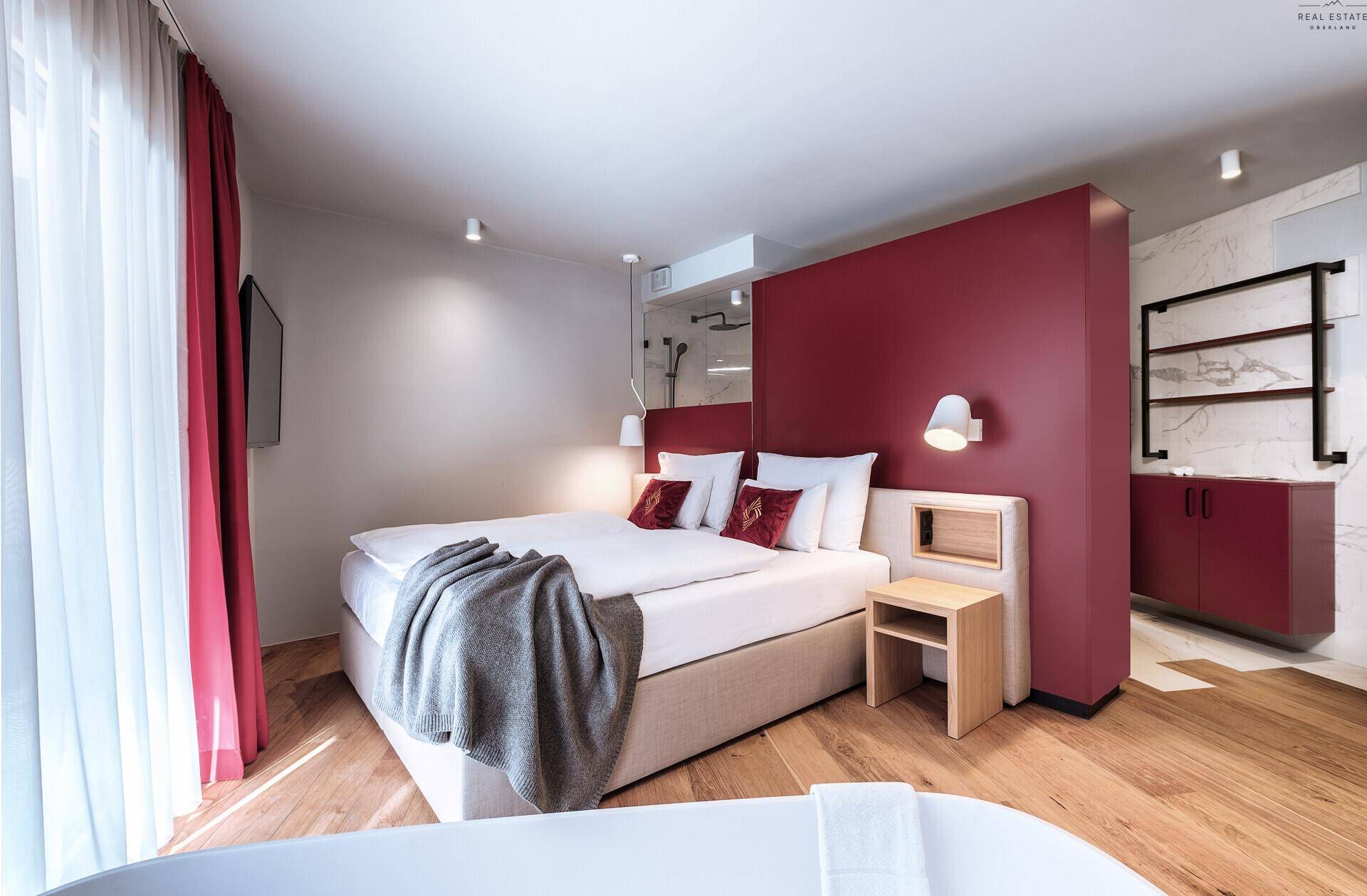 Helles Schlafzimmer mit Holzboden, roter Akzentwand und moderner Einrichtung.