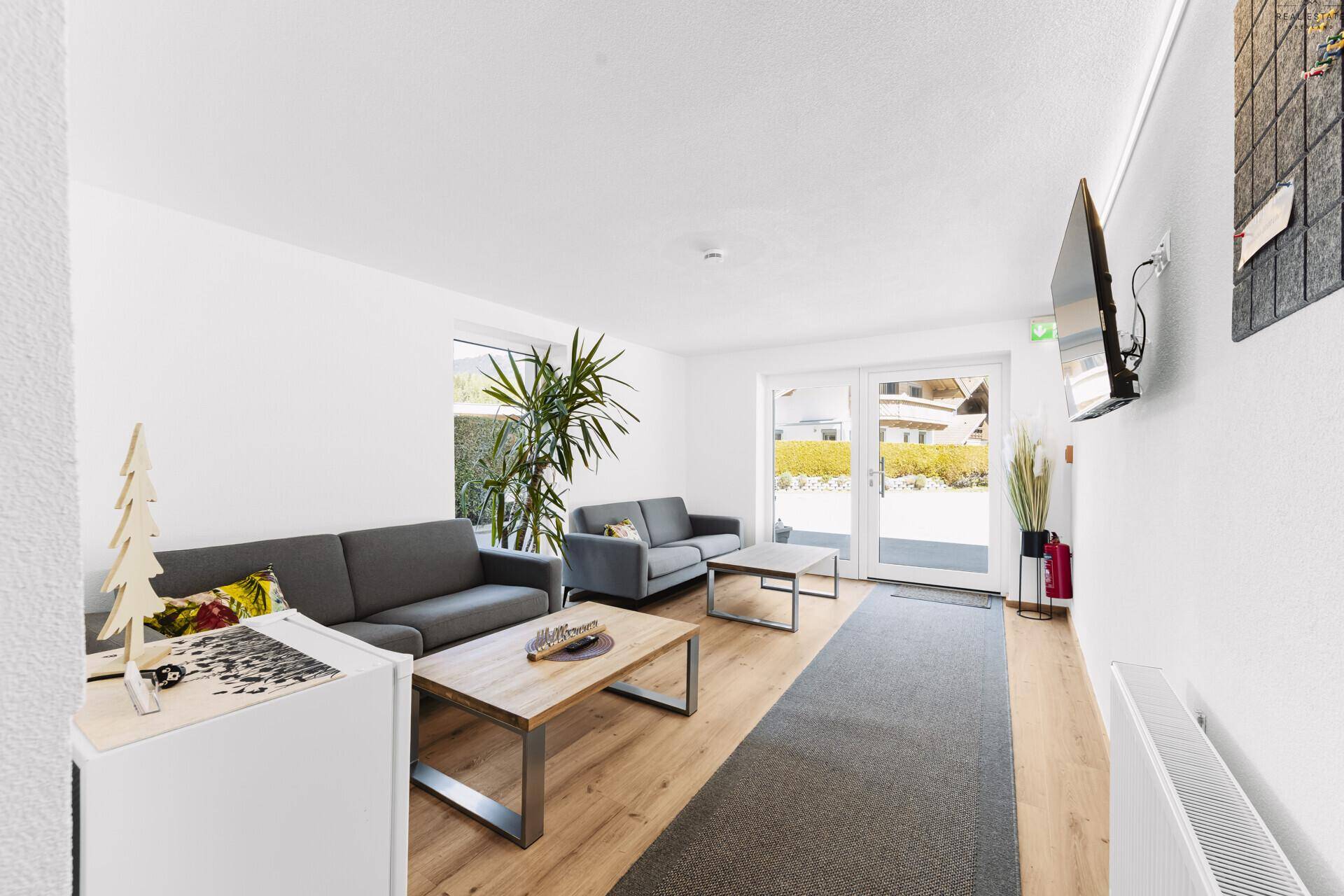 Helles Wohnzimmer mit Holzboden, modernen Sofas und Zugang zum Außenbereich durch Glastüren.