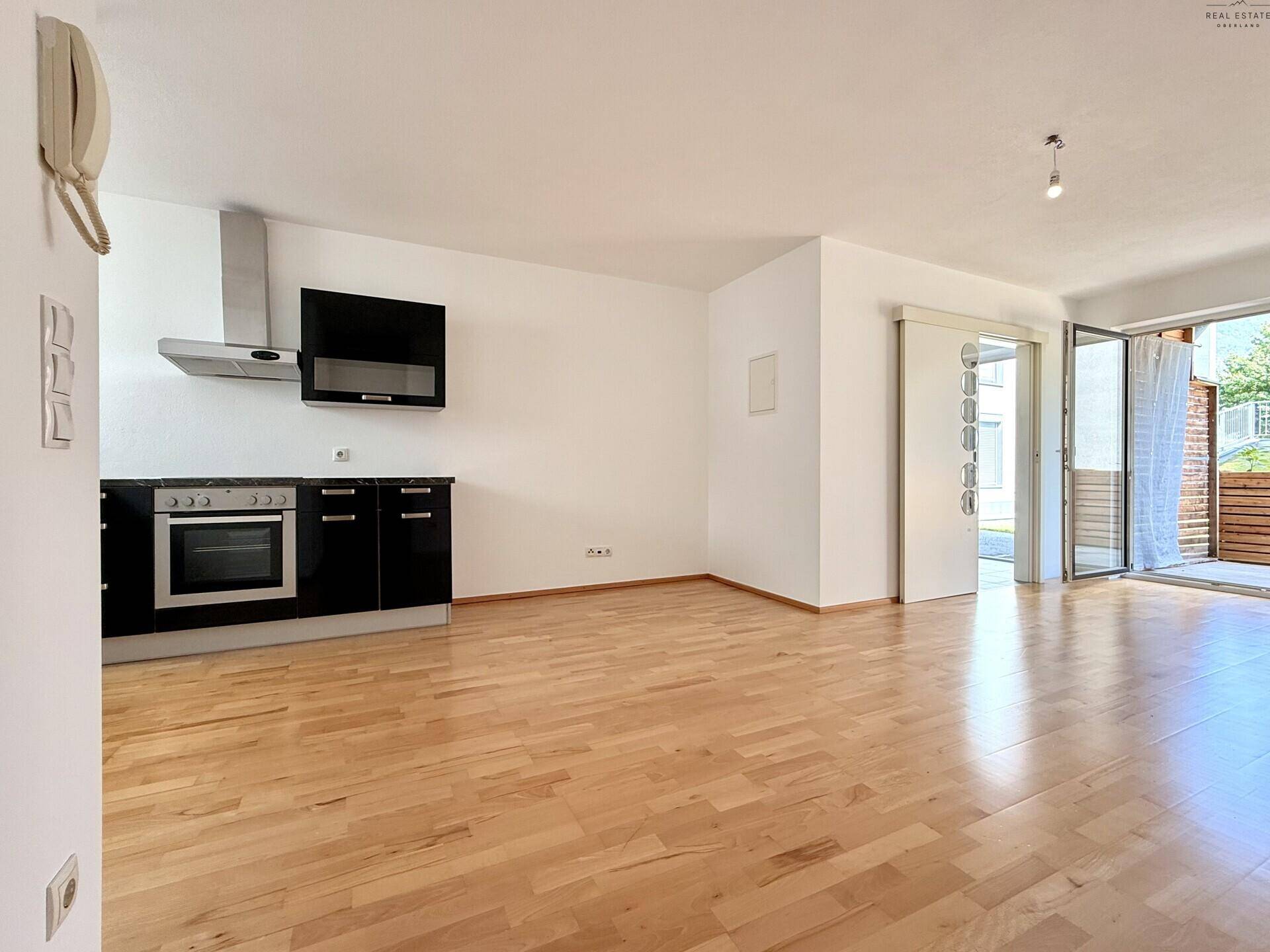 Offener Wohnbereich mit Holzboden, integrierter Küchenzeile und Zugang zur Terrasse.