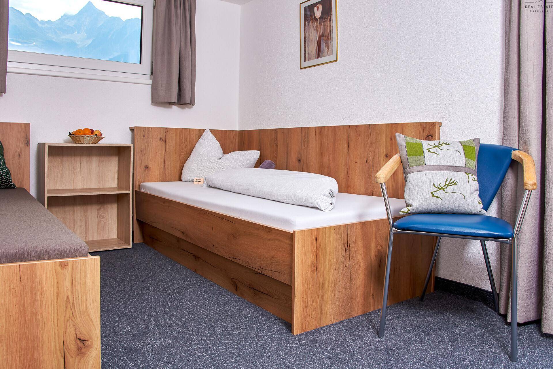 Helles Schlafzimmer mit Einzelbett, Holzbettrahmen und einem Fenster mit Bergblick.