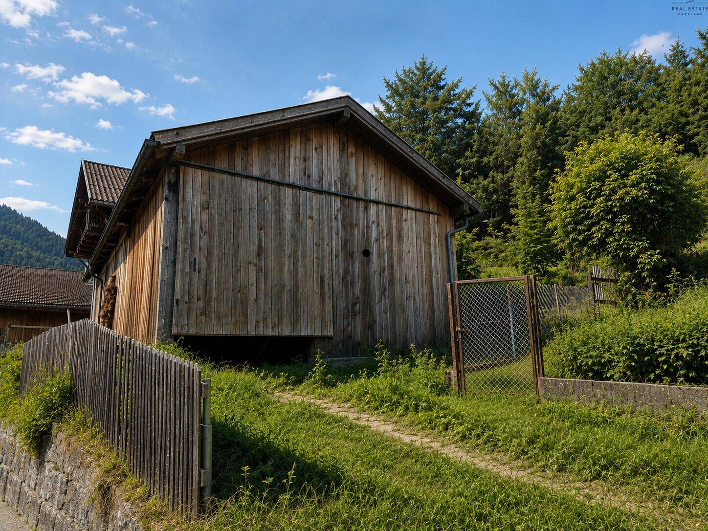 Rustikales Holzgebäude mit Zaun und grüner Wiese, umgeben von Bäumen.