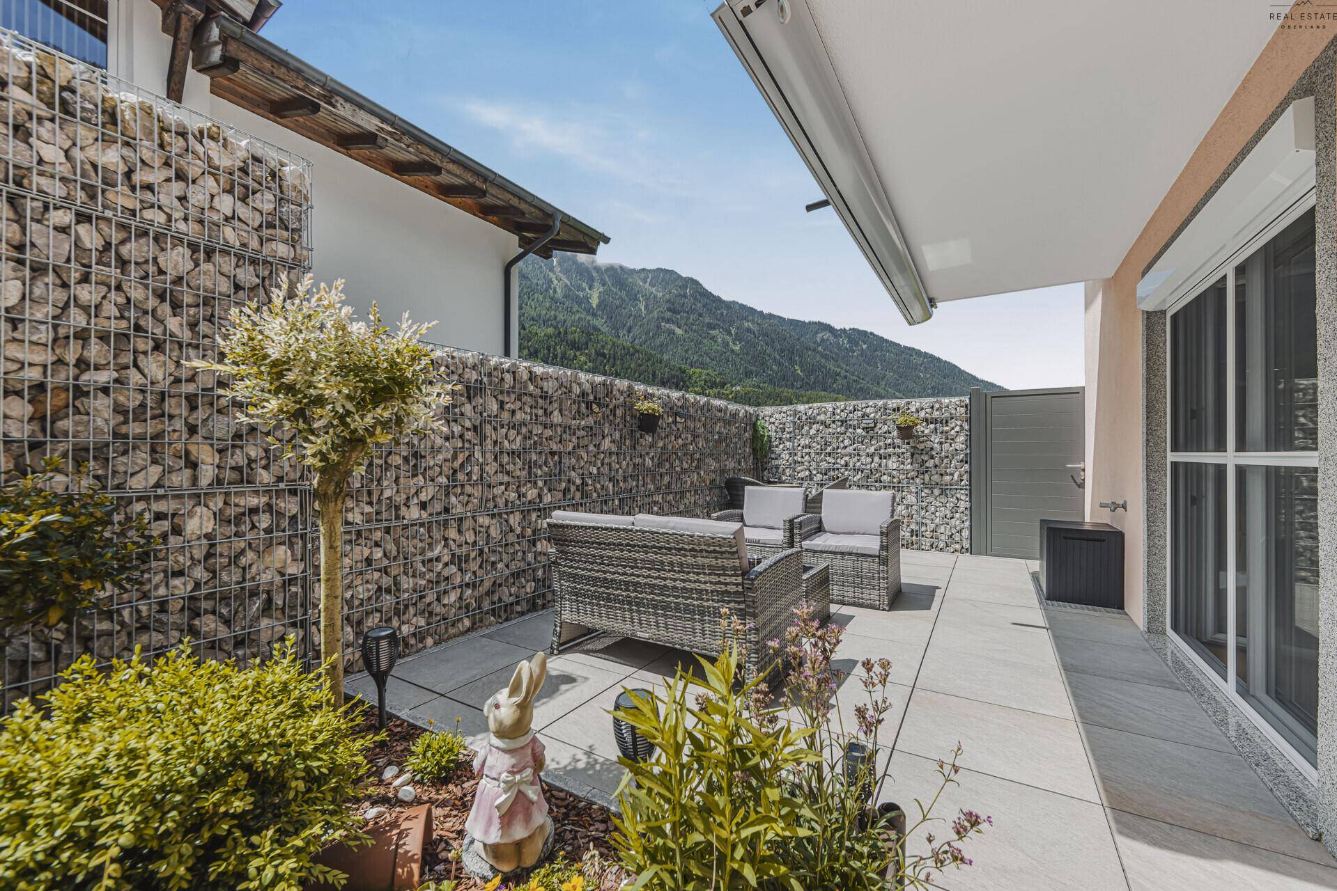 Gepflegte Terrasse mit Pflanzen, Gartenfiguren und weitem Blick auf die Berge.