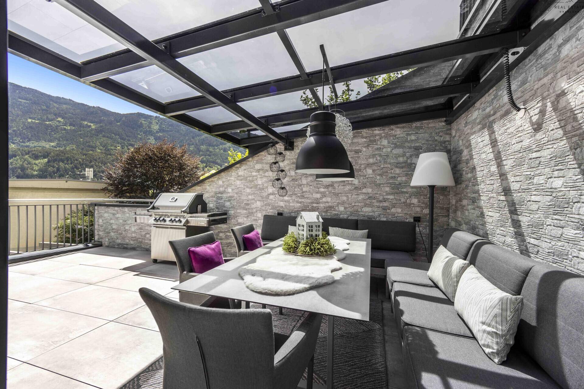 Überdachte Außenterrasse mit Essbereich, Lounge-Sofa, Grill und Bergblick.
