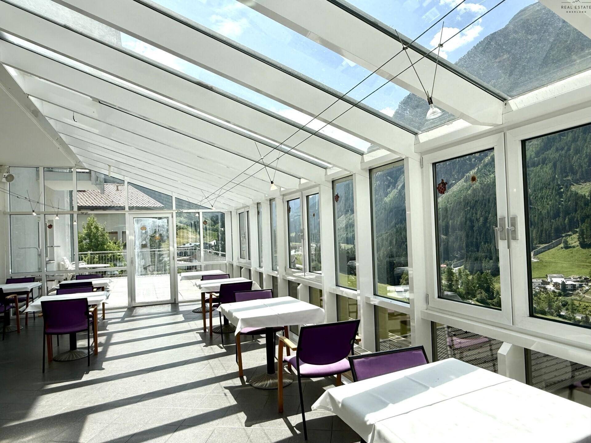 Heller Speisesaal im Wintergarten mit Glasdach und weitem Blick auf die alpine Landschaft.