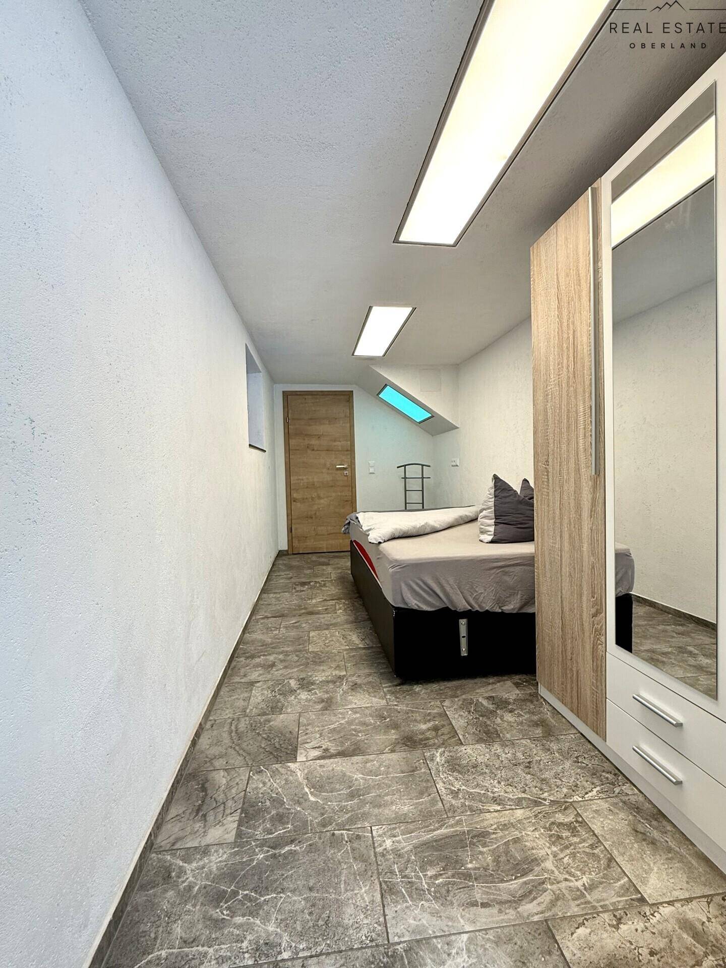 Schlafzimmer im Untergeschoss mit Fliesenboden, Kleiderschrank und Dachfenster.