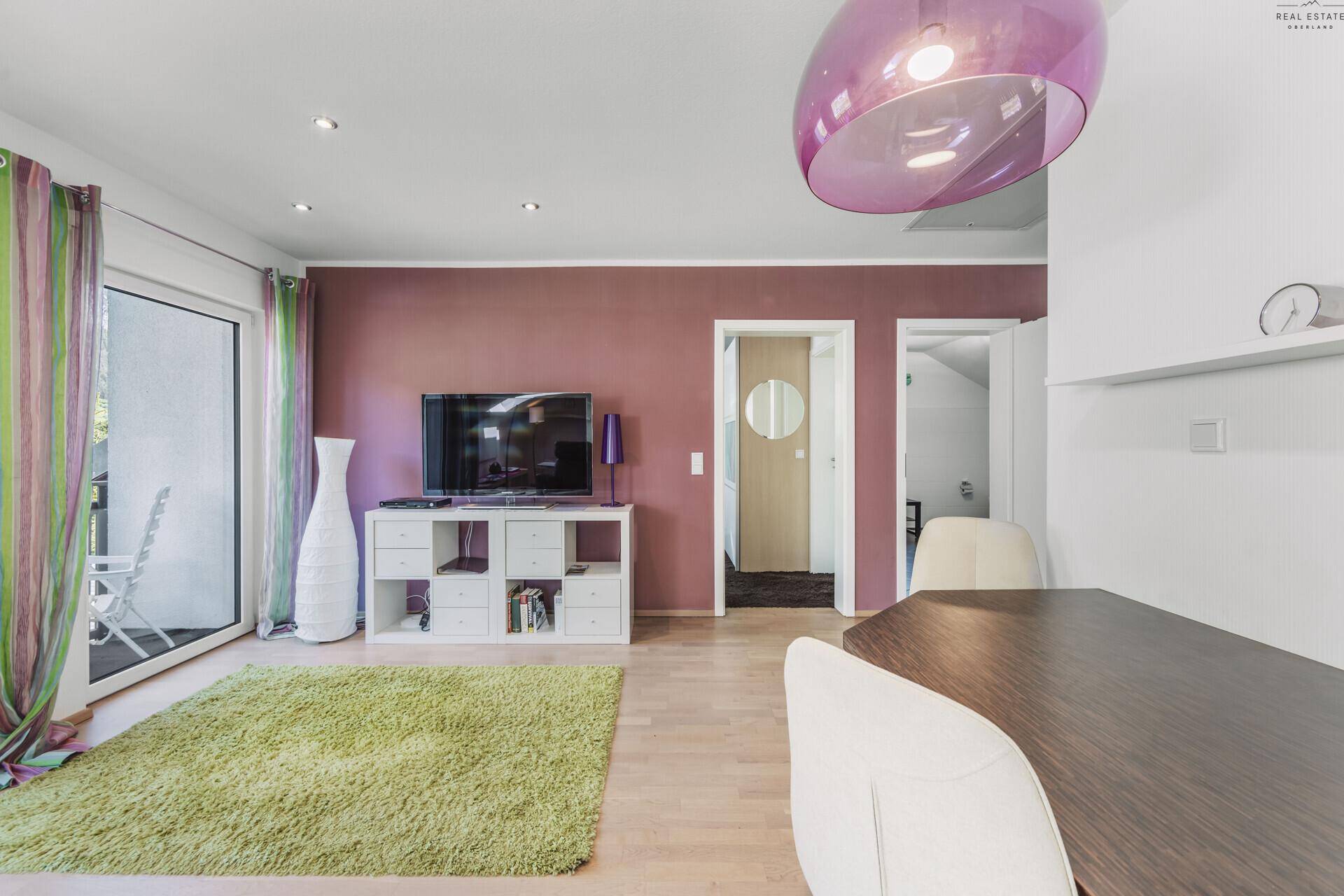 Wohnzimmer in der Dachgeschosswohnung mit Balkonzugang, Fernseher und moderner Einrichtung.