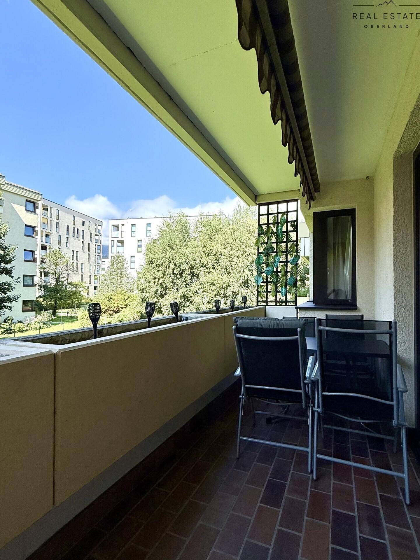 Balkon mit Sitzgelegenheiten, Markise und Blick auf die grüne Umgebung.