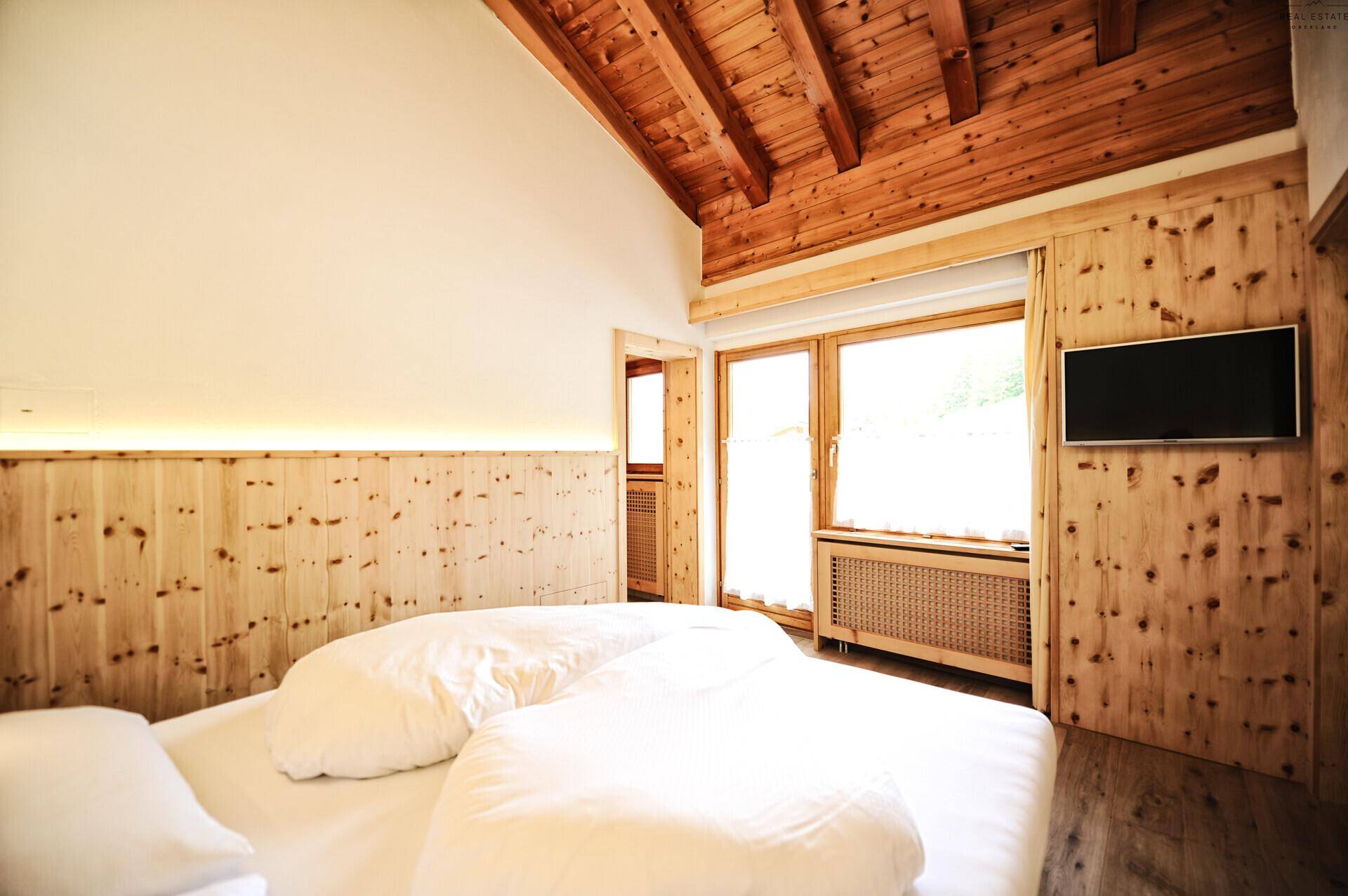 Gemütliches Schlafzimmer mit sichtbaren Holzbalken an der Decke, Holzvertäfelung und einem großen Fenster.