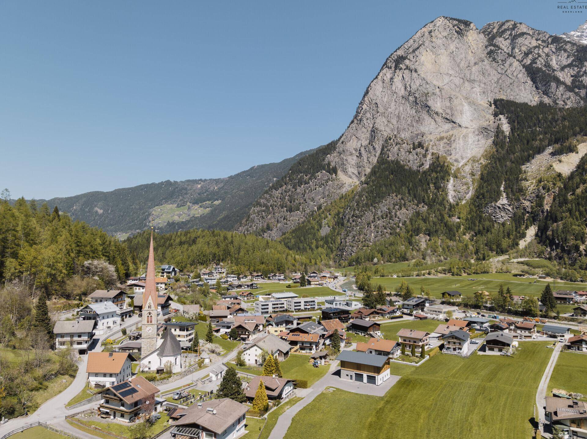 Panoramablick auf ein idyllisches Dorf mit Kirche, eingebettet in eine beeindruckende Berglandschaft.
