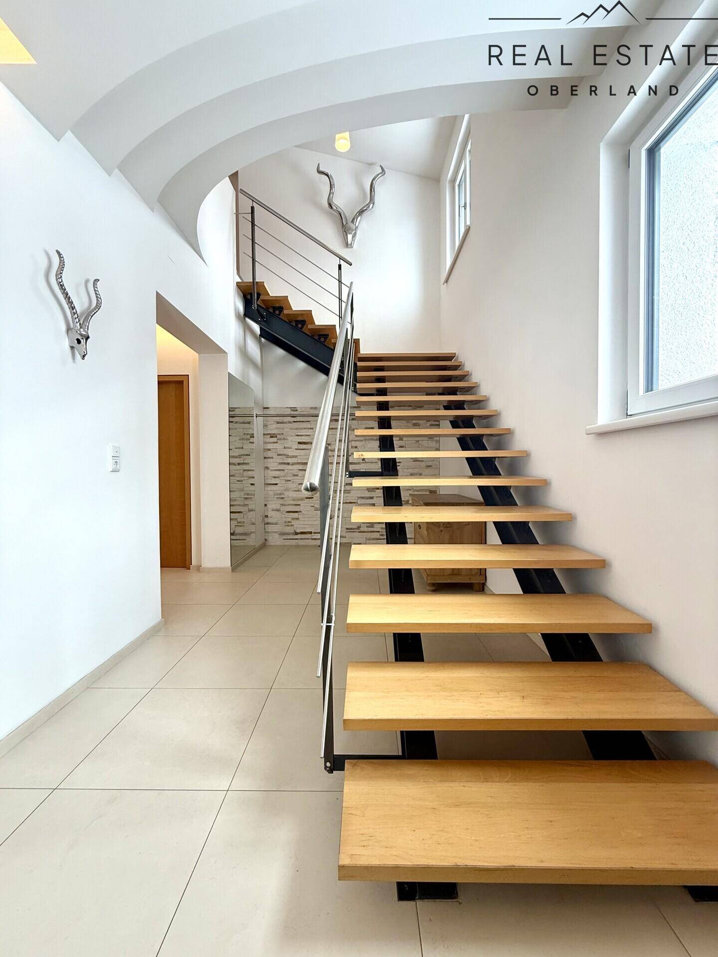 Elegante Holztreppe mit Metallgeländer und hellem Fliesenboden, die das moderne Design unterstreicht.