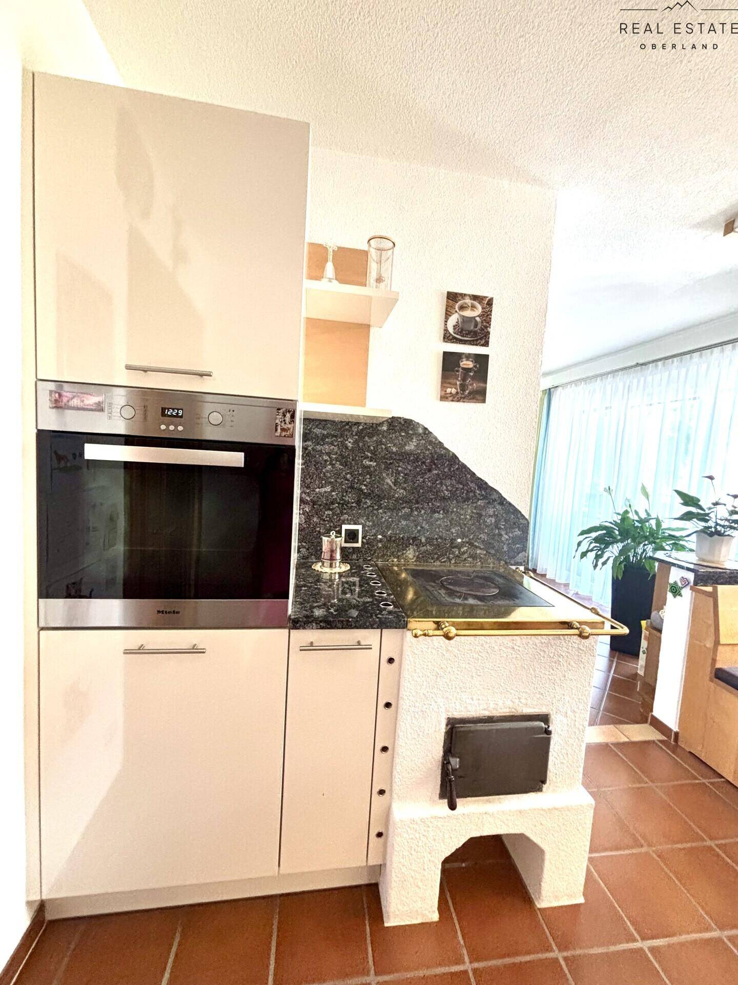 Küchenzeile mit integriertem Backofen, Kochfeld und einem traditionellen Kachelofen als Heizelement.